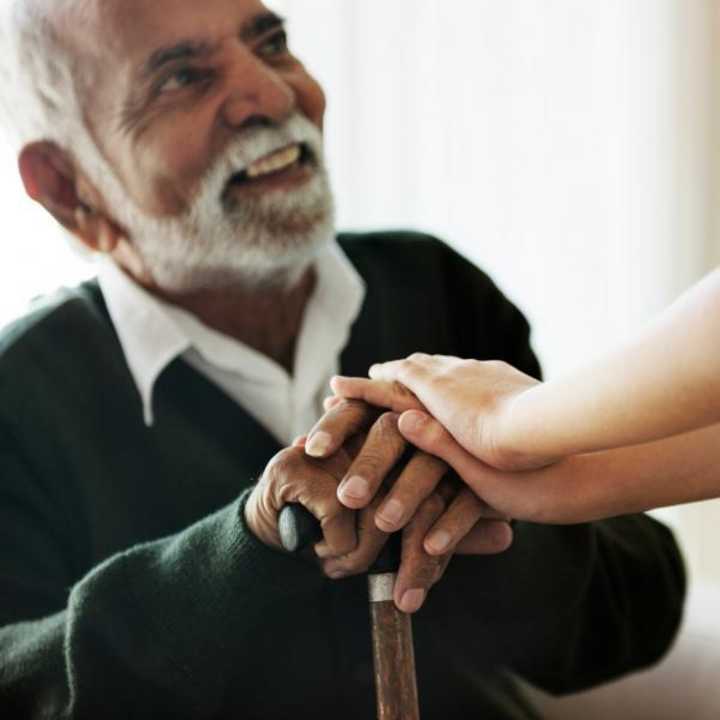 Elderly man with a walking stick being reassured by carer 