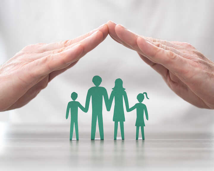 hands held over a carboard cut-out of a family protecting them