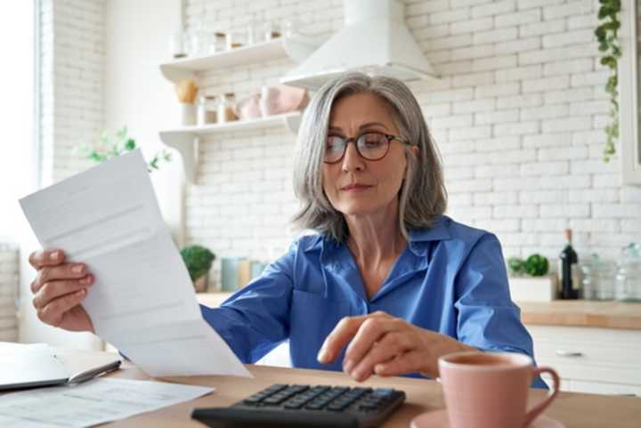 Mature business woman with paperwork and a calculator at the kitchen table