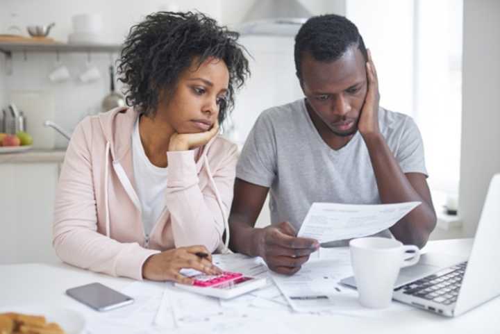 A young couple sitting at the kitchen table with bills, laptop and calculator