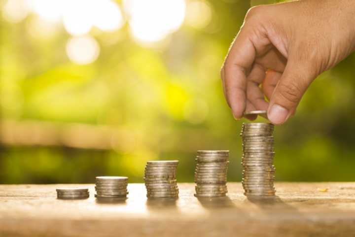 A hand adding money to a pile of coins