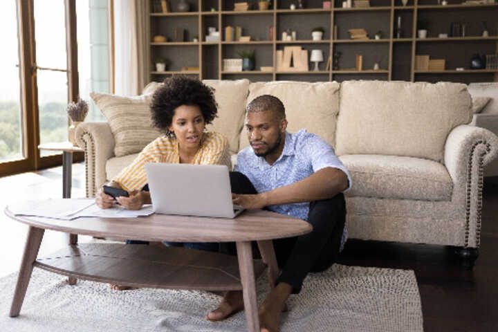 Young couple in their living room, looking at a laptop with bills and a calculator