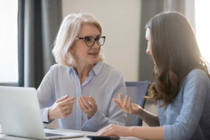 Mature woman and younger woman having a discussion, with laptop on desk