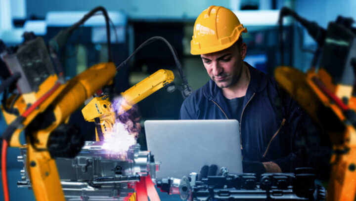 Worker with hard hat looking at a laptop in a modern factory