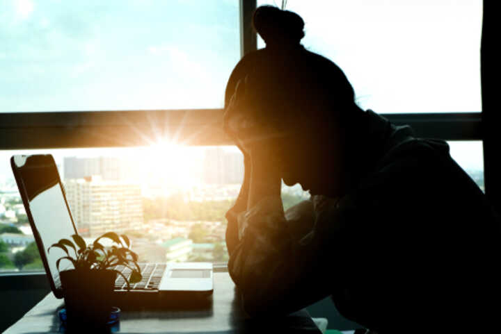 Stressed woman sitting at her laptop, with city view outside the window