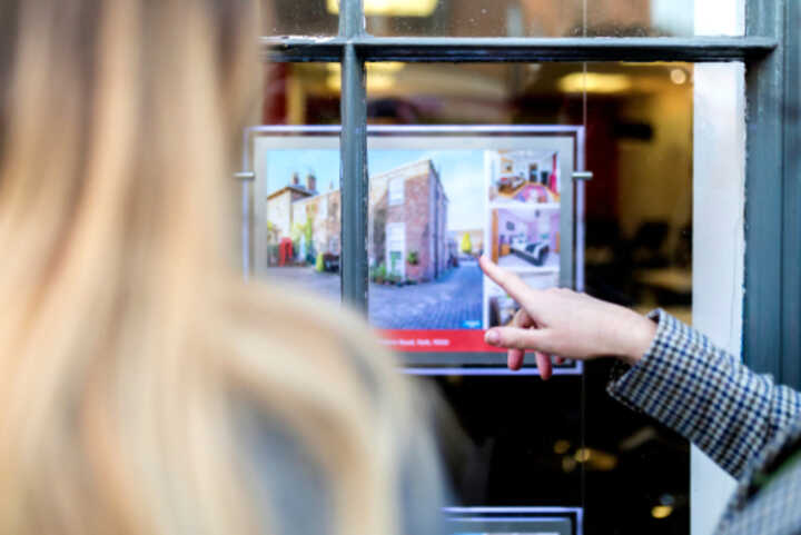 Couple looking at a property advert in the window of an estate agents