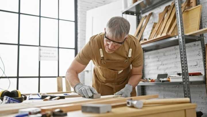 A mature man working in a carpentry workshop surrounded by wood and tools