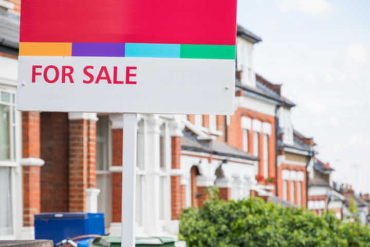 Estate agent's 'For Sale' sign outside a terraced house