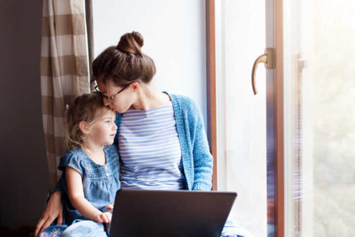 A mother working on a laptop turns to embrace her young daughter