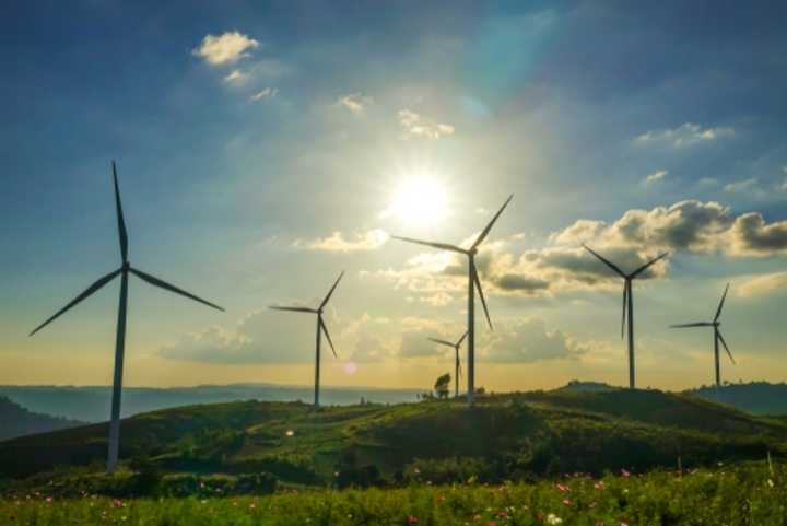 Wind turbines on a grassy hill, with bright sunshine and blue sky