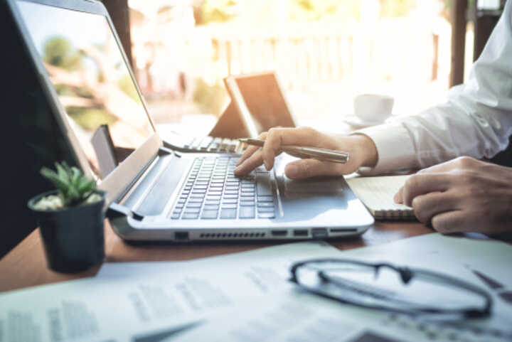 Person working at a laptop, with paperwork and a pen